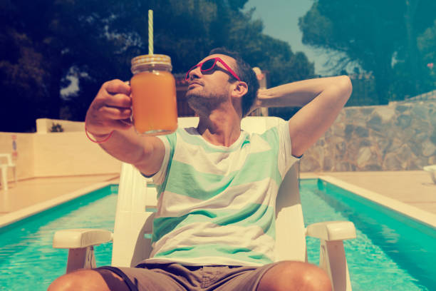 Young man on the swimming pool holding jar with orange juice.