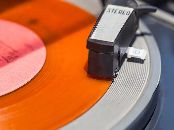 Photo of tonearm of record-player on orange vinyl disc