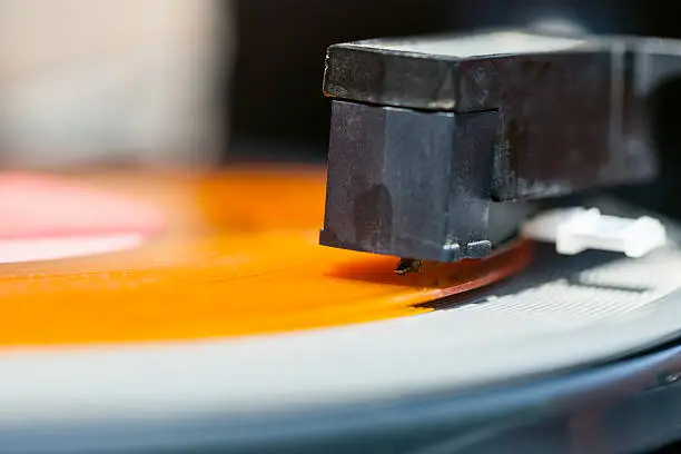 Photo of stylus of headshell on orange vinyl record