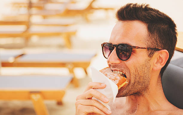 istock Young handsome man eating donut on the beach 545431910