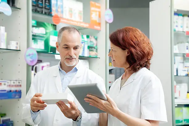 Two pharmacists, mature man and woman, working.