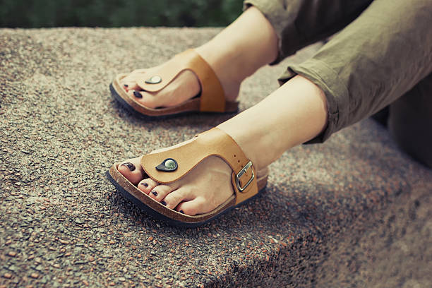 Woman's feet in yellow stylish summer sandals Woman's feet in yellow stylish summer sandals with dark nail polish, in green summer pants sitting on the wall flat shoe photos stock pictures, royalty-free photos & images