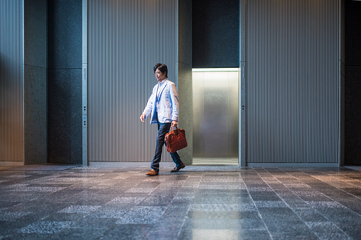 Japanese businessman walking out of elevator in the entrance hall of an office building.