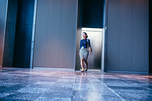 Japanese businesswoman walking out of elevator in the entrance hall of an office building.