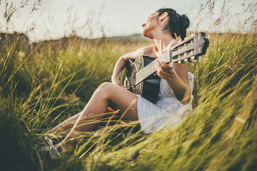 beautiful young woman with braided hair playing guitar on the meadow