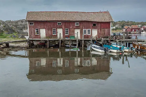 An old building and dock on the Swedish island of South Koster is surrounded by a dock and small fishing boats.  The scene is reflected in the foreground.  The island is, with few exceptions, vehicle free.