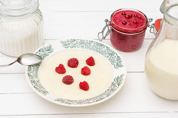  Semolina porridge with raspberries ,jar with milk and jam for breakfast on the white wooden table  