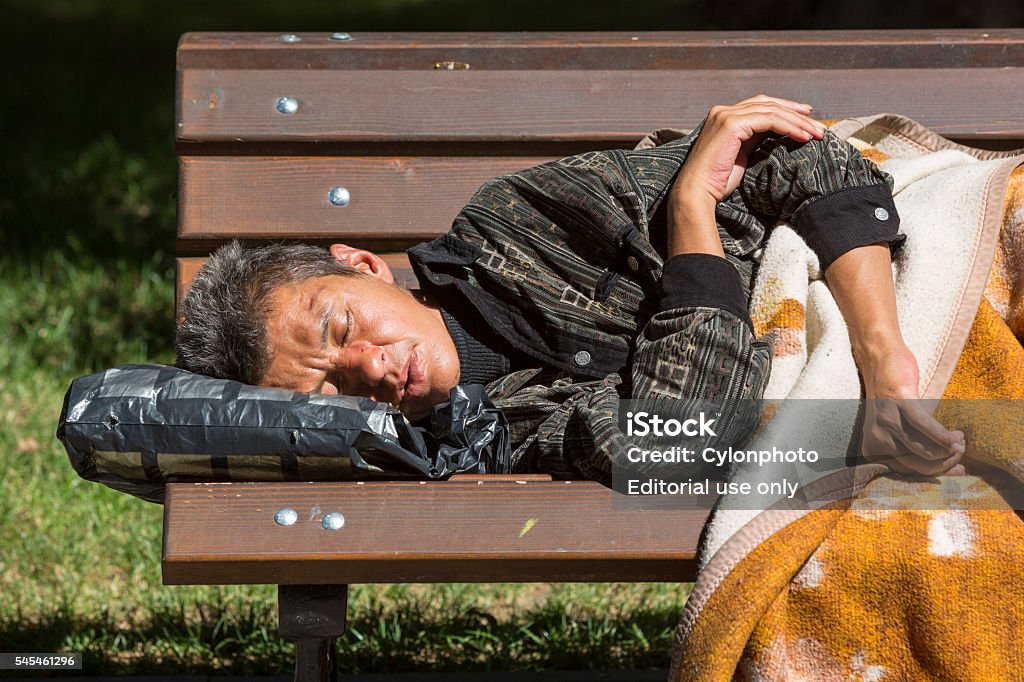 Homeless woman sleeping on a bench Sofia, Bulgaria - July 6, 2016: Homeless woman is sleeping on a bench in a park wrapped in blanket in the center of Sofia. Years after joining the EU Bulgaria is still the poorest country in the union. Abandoned Stock Photo