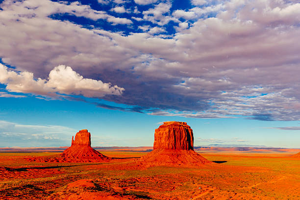 Fluffy clouds over a desert landscape with The Mittens rock formation.