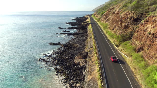 AERIAL: Red convertible driving along the picturesque coastal road