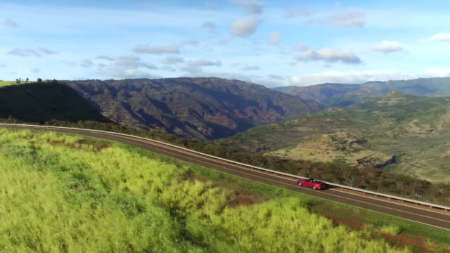 AERIAL: Red convertible driving on the edge of amazing majestic canyon in Hawaii