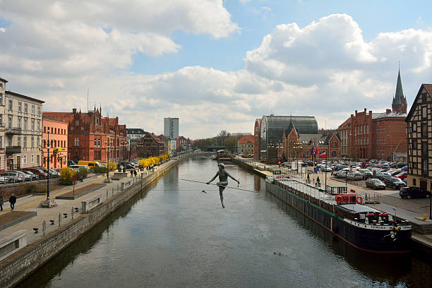 Bydgoszcz, Poland – April 6, 2016. View of Brda river front in Bydgoszcz, Poland, with ropewalker sculpture, residential buildings, commercial shops, the Main Post Office, cars and people.