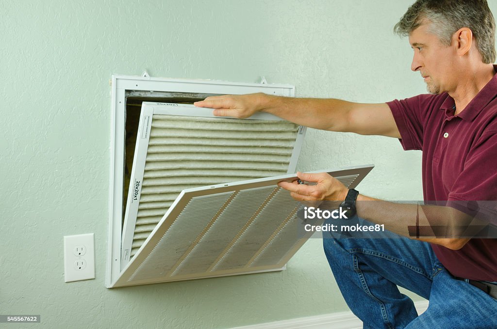 Home owner replacing air filter on air conditioner Professional repair service man or diy home owner removing a dirty air filter on a house air conditioner so he can replace it with a new clean one. Air Duct Stock Photo