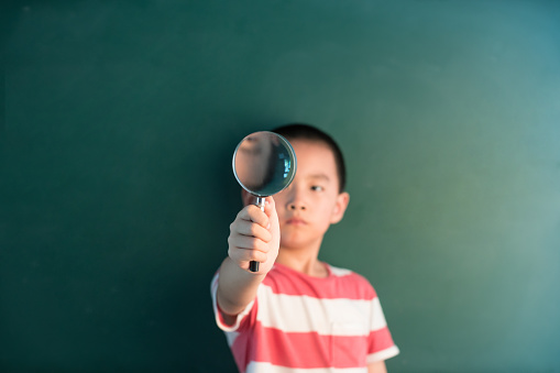 asian boy standing infront of chalkboard with magnifier