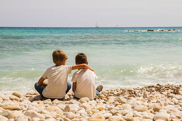 istock Two boys sitting together on the beach and looking at 545569758