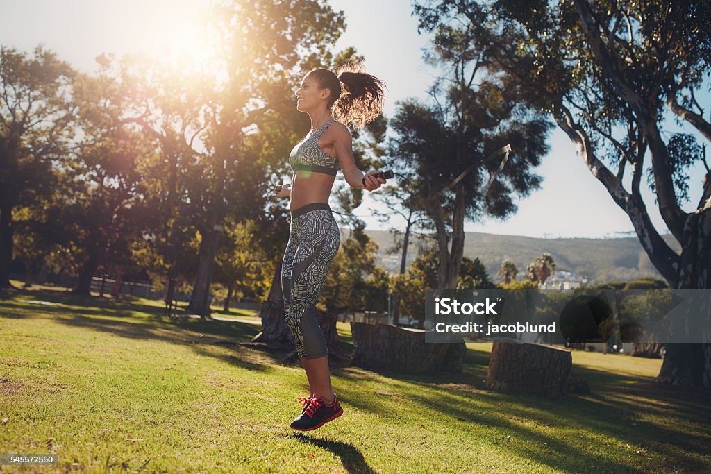 Sporty woman skipping in a park Side view of sporty woman skipping in a park on a sunny morning. Fit and athletic female exercising with a jump rope on the grass. Jump Rope Stock Photo