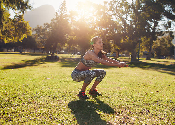 Full length outdoor shot of fit young woman exercising in park. She doing squatting on a sunny morning.