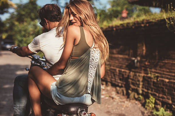 Rear view of attractive young female with her boyfriend on a motorcycle. Couple enjoying motorbike ride on countryside road.