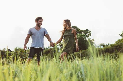 Shot of happy young couple walking in the meadow. Man and woman holding hands and walking together in field of tall grass.