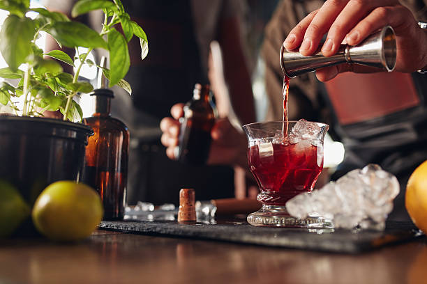Bartender preparing fresh cocktail Close up shot of barman hand pouring drink from measuring cup into a cocktail glass filled with ice cubes. Male bartender preparing fresh cocktail. jigger pour stock pictures, royalty-free photos & images
