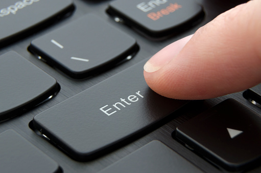 Finger pushing enter button on black computer keyboard; Macro photo