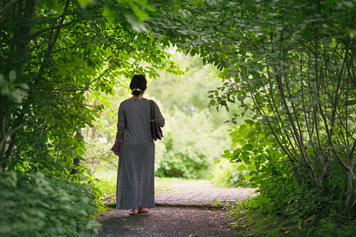 A middle aged woman walking through a tunnel of leaves in a peaceful and green summer garden.
