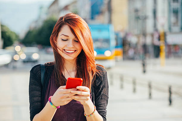 Happy city girl texting Smiling young woman with smart phone checking messages outdoors at urban setting, with copy space dyed red hair photos stock pictures, royalty-free photos & images