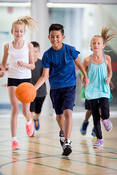 Elementary Students Playing Basketball A group of children are plying basketball together in the gym during summer day camp. youth basketball indoor stock pictures, royalty-free photos & images