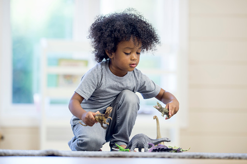 A cute little boy is playing with plastic toys on the floor during preschool.