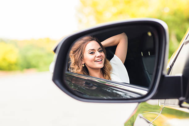istock Happy young woman driver looking in car side view mirror 545642090
