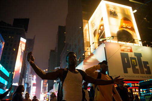 New York City, USA - July 9, 2016: Black Lives Matter protestors march down a street in Times Square in New York City, demonstrating against police violence. One man marches with arms outstetched, a crucifix in one hand.