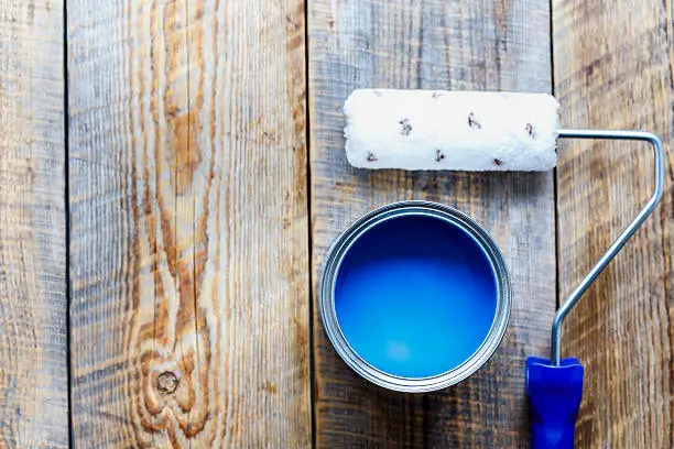 painting with can of blue paint and roller top view on wooden background