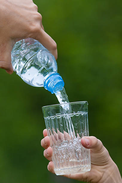 istock hand pouring water from bottle into glass on green backgroun 545652960