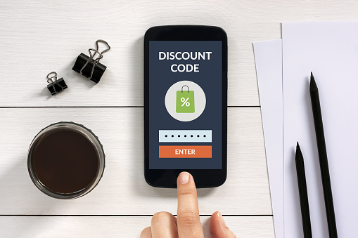 Discount code concept on smart phone screen with office objects on white wooden table. All screen content is designed by me.