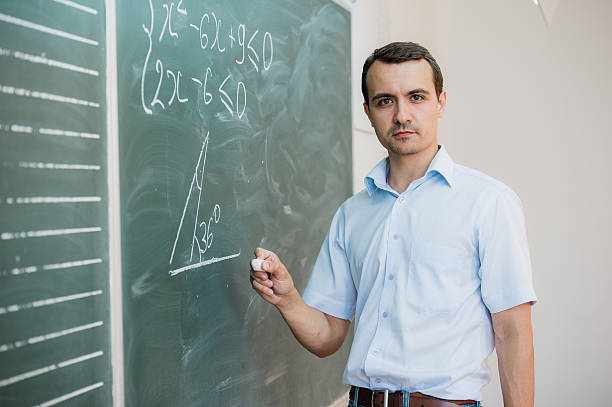 istock Young male teacher or student holding chalk writing on chalkboard 545655170