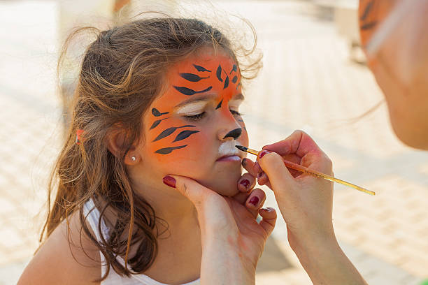 Girl getting her face painted by painting artist. stock photo
