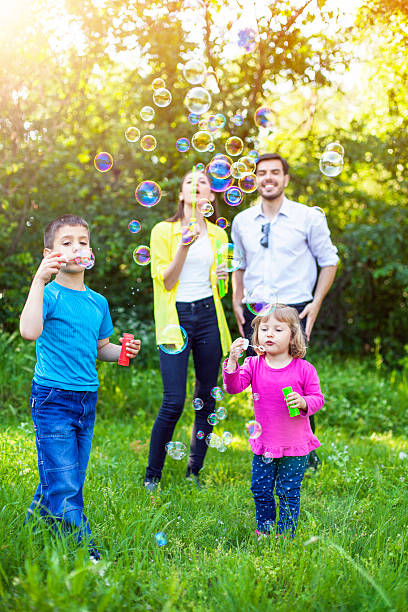 famille heureuse jouant avec soap bubbles - bubble wand outdoors little boys mother photos et images de collection