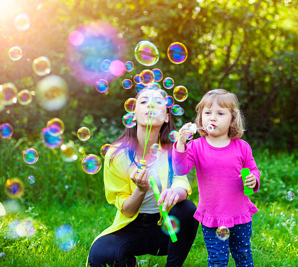 madre feliz y su hijo jugando con pompas de jabón - bubble child bubble wand blowing fotografías e imágenes de stock