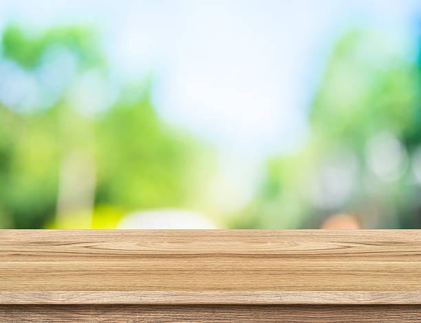 istock Empty wood table top with sun and blur tree bokeh 545675934