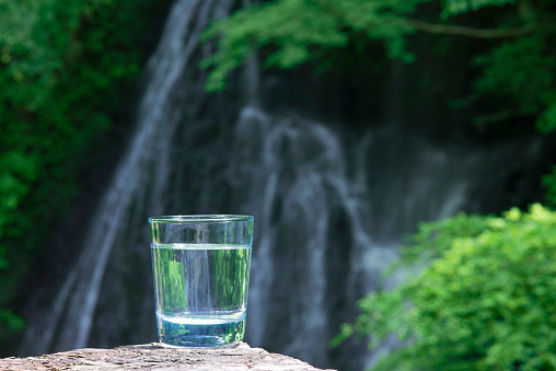 \nA glass of fresh and cold natural water . It was shot in the vicinity of the waterfall of the valley  in Japan.