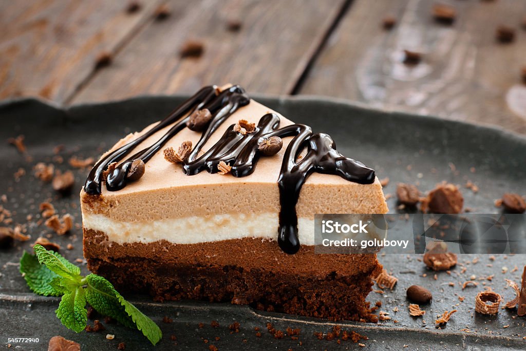 Peace of layered sweet chocolate souffle dessert Peace of layered souffle dessert with chocolate sauce on black plate with mint leaves, on blurred wooden table Dessert - Sweet Food Stock Photo