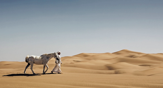 An Arab is walking his horse through the desert.