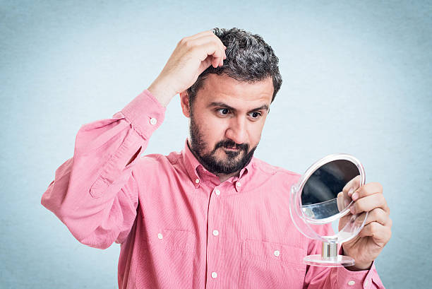 istock Man worried about gray hair looking in a mirror 545776732