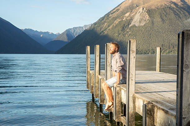 istock Man sits on lake pier, enjoys mountain lake landscape 545796740