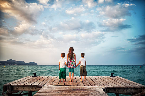 Brothers and sister looking at sea from pier. Summer vacations day evening.