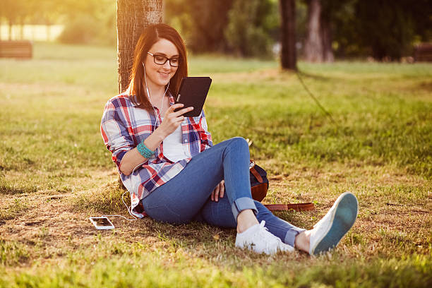 femme dans le parc lisant un livre électronique - women grass glasses e reader photos et images de collection