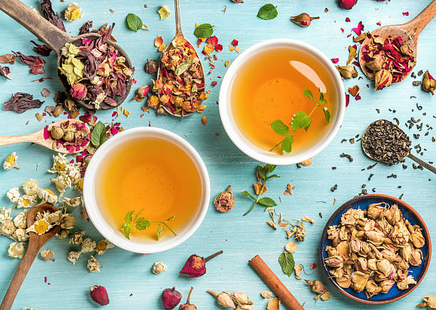 Two cups of healthy herbal tea with mint, cinnamon, dried Two cups of healthy herbal tea with mint, cinnamon, dried rose and camomile flowers in spoons over blue background, top view foxys_forest_manufacture stock pictures, royalty-free photos & images