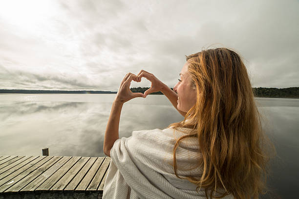 istock Woman makes heart shape finger frame to mountain lake landscape 545803836