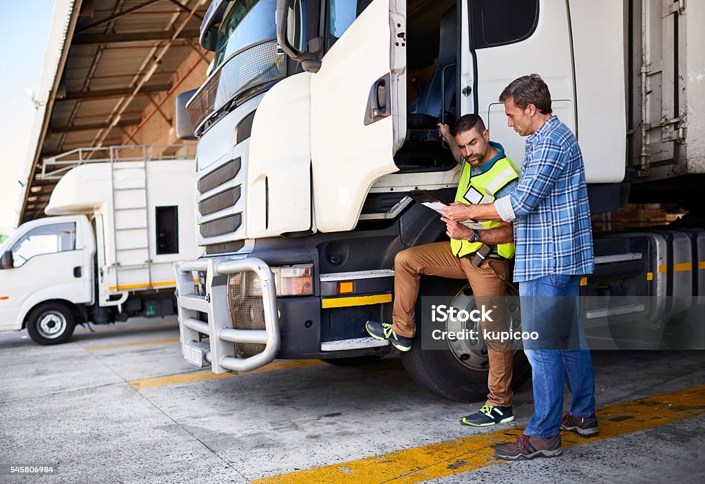 Checking the manifest one last time Shot of two coworkers talking together next to a large truck outside of a distribution center Truck Stock Photo