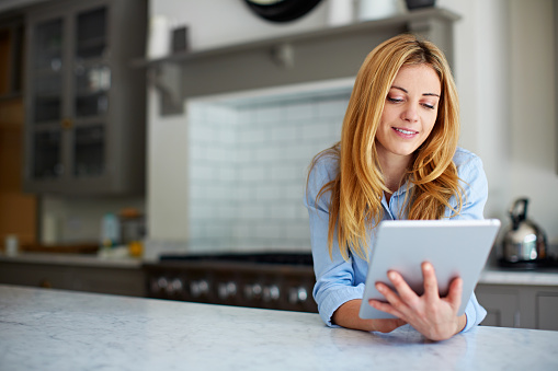 Shot of a young woman leaning on her counter at home using a digital tablet